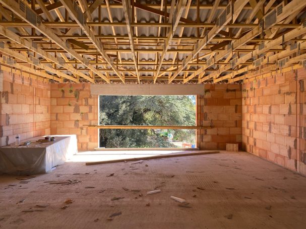 Intérieur d'une pièce en construction, murs en briques, vue sur l'extérieur à travers une grande fenêtre.