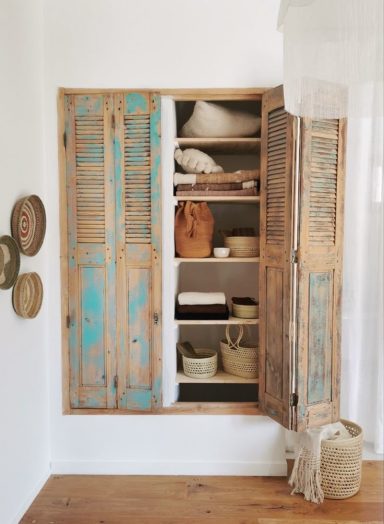 Armoire en bois aux portes bleuies, remplie de paniers et d'objets décoratifs.