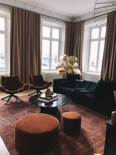 Salon moderne avec canapés sombres, fauteuils orange et table noire. Éclairage naturel.