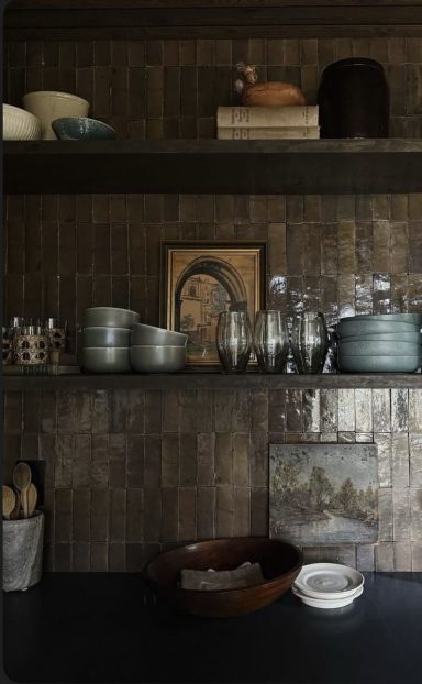 Étagère de cuisine avec vaisselle, bocaux et une image encadrée sur fond sombre.