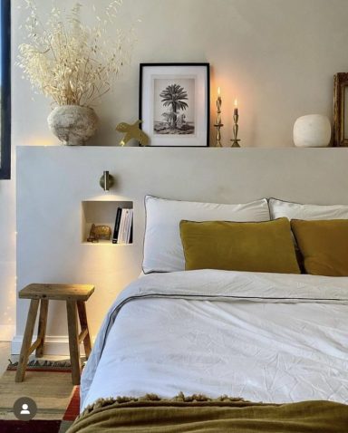 Chambre lumineuse avec lit, coussins verts, décor minimaliste et plantes sèches.