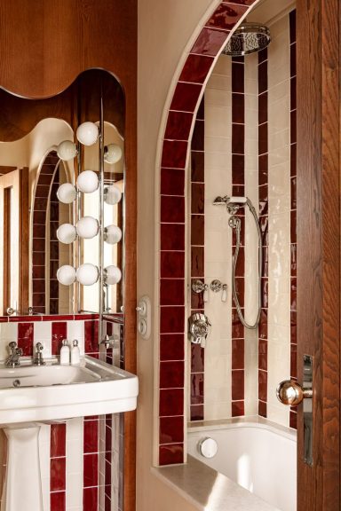 Salle de bain élégante avec carrelage rouge, douche moderne et miroir lumineux.